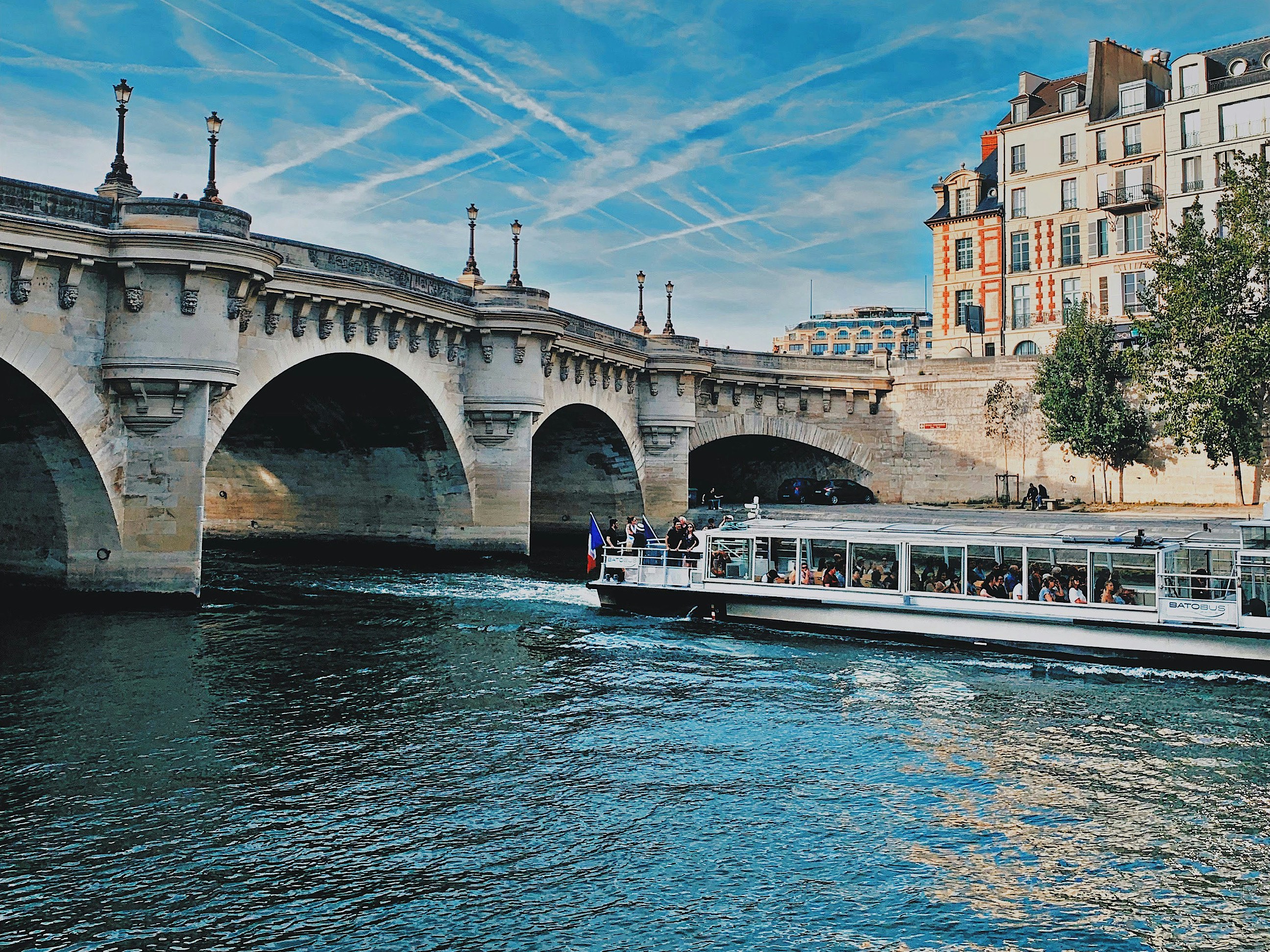 A small long boat glides alond the river under a bridge.